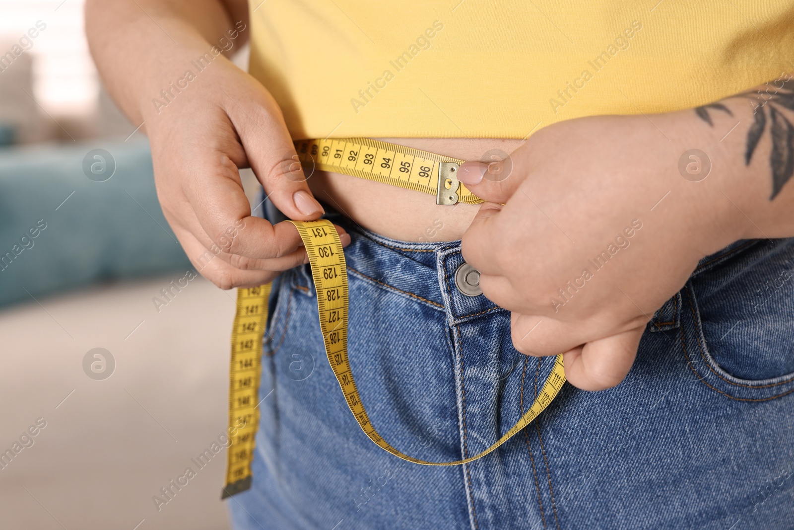 Photo of Weight loss. Plus size woman measuring waist with tape at home, closeup