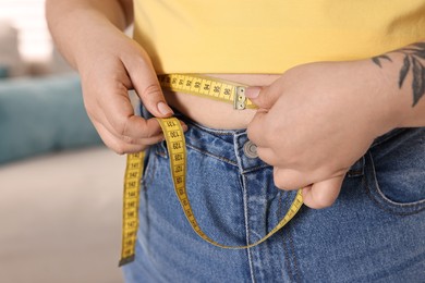 Photo of Weight loss. Plus size woman measuring waist with tape at home, closeup