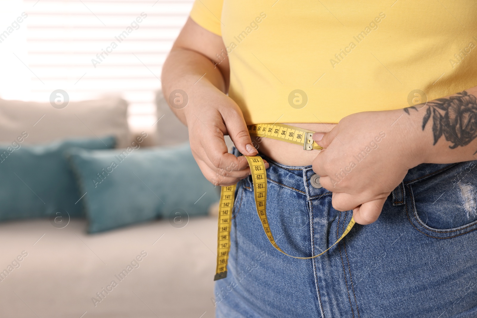 Photo of Weight loss. Plus size woman measuring waist with tape at home, closeup. Space for text