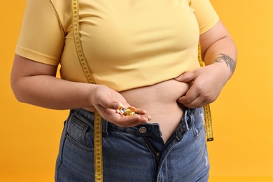 Photo of Plus size woman with pile of weight loss supplements on orange background, closeup