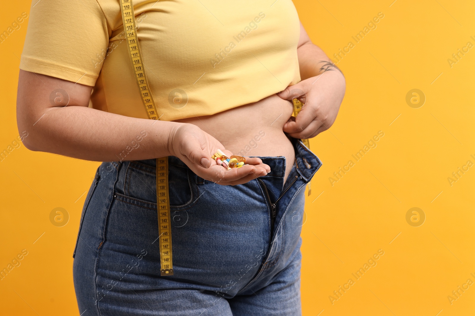 Photo of Plus size woman with pile of weight loss supplements on orange background, closeup