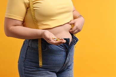 Photo of Plus size woman with pile of weight loss supplements on orange background, closeup