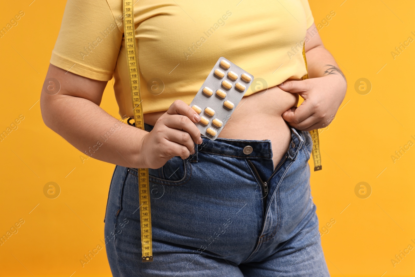 Photo of Plus size woman with blister of weight loss supplements on orange background, closeup