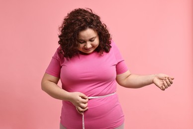 Photo of Weight loss. Happy plus size woman measuring waist with tape on pink background