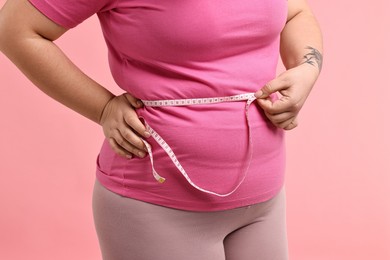 Photo of Weight loss. Plus size woman measuring waist with tape on pink background, closeup