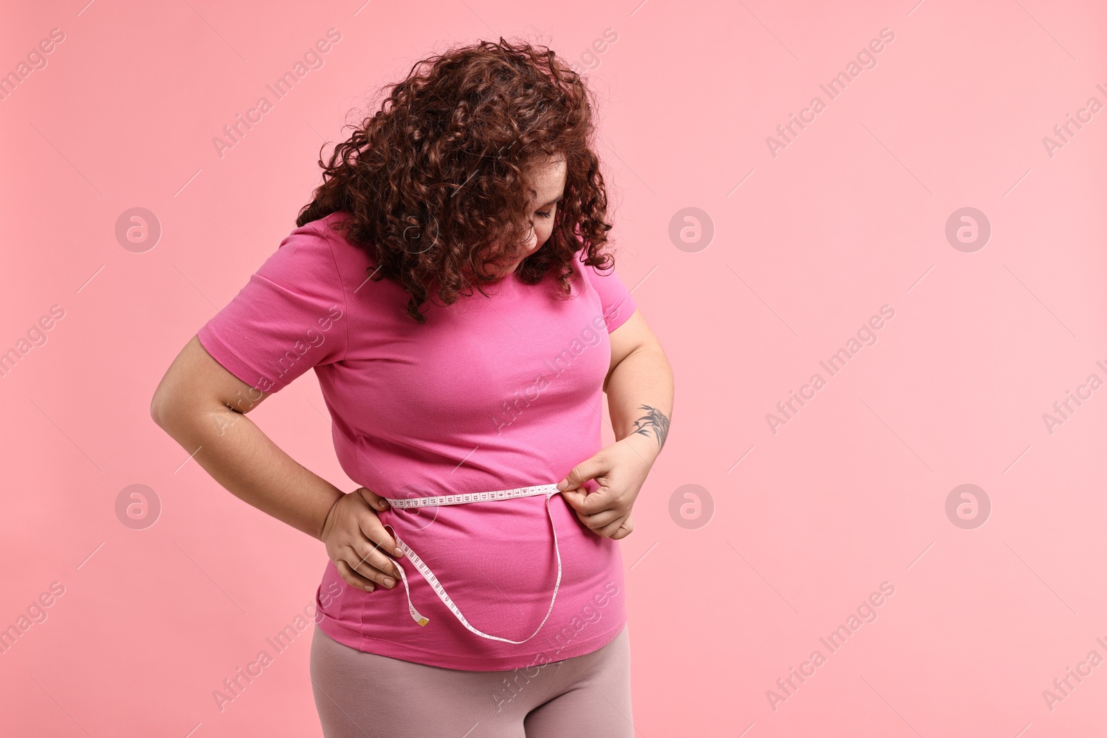 Photo of Weight loss. Plus size woman measuring waist with tape on pink background