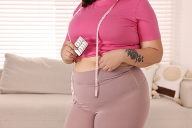 Photo of Plus size woman holding blister of weight loss supplements at home, closeup. Space for text