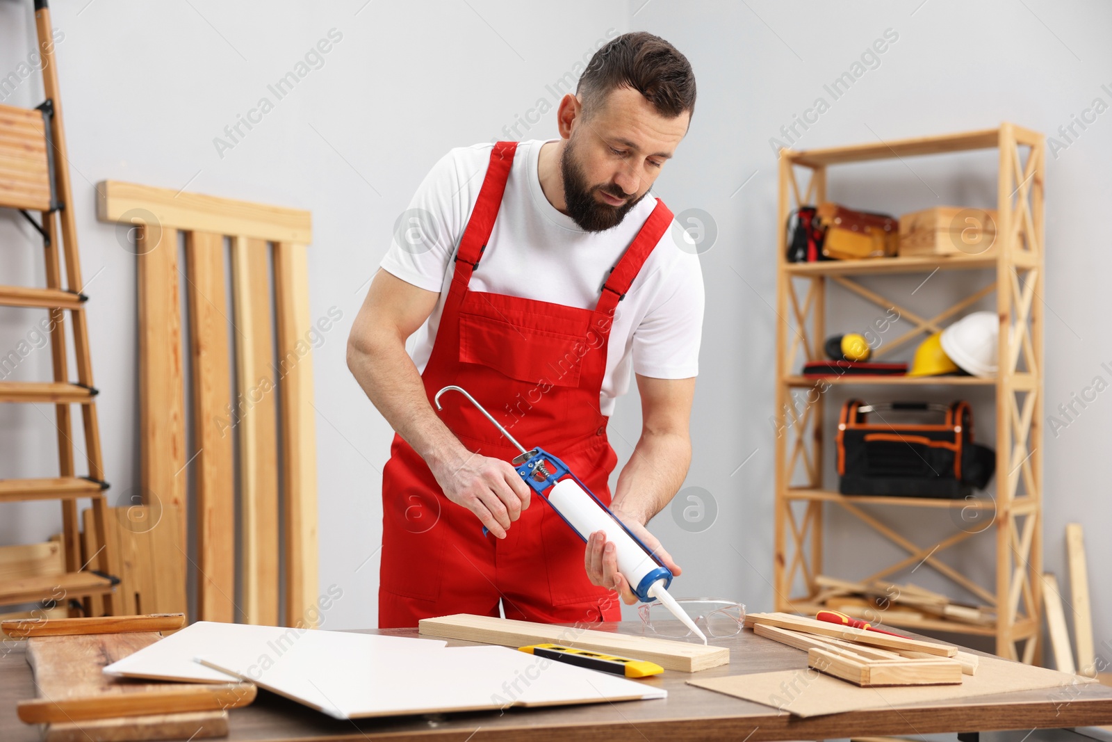 Photo of Worker with caulking gun glueing wooden plank indoors