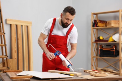 Photo of Worker with caulking gun glueing wooden plank indoors