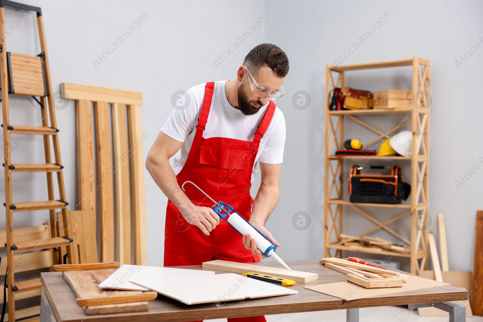 Photo of Worker with caulking gun glueing wooden plank indoors