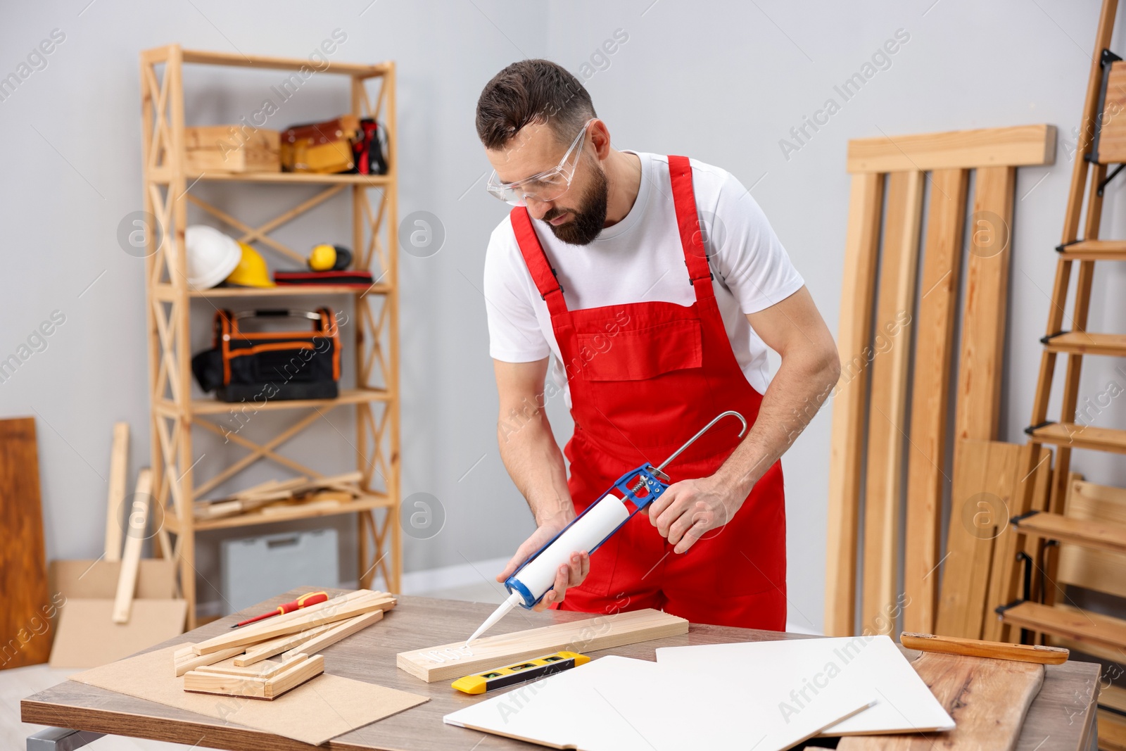 Photo of Worker with caulking gun glueing wooden plank indoors