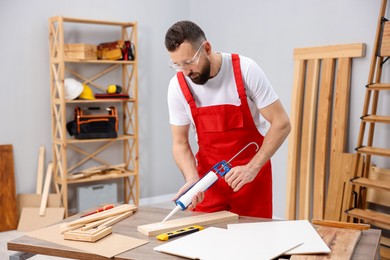 Photo of Worker with caulking gun glueing wooden plank indoors