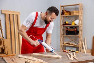 Photo of Worker with caulking gun glueing wooden plank indoors