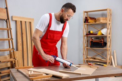 Photo of Worker with caulking gun glueing wooden plank indoors