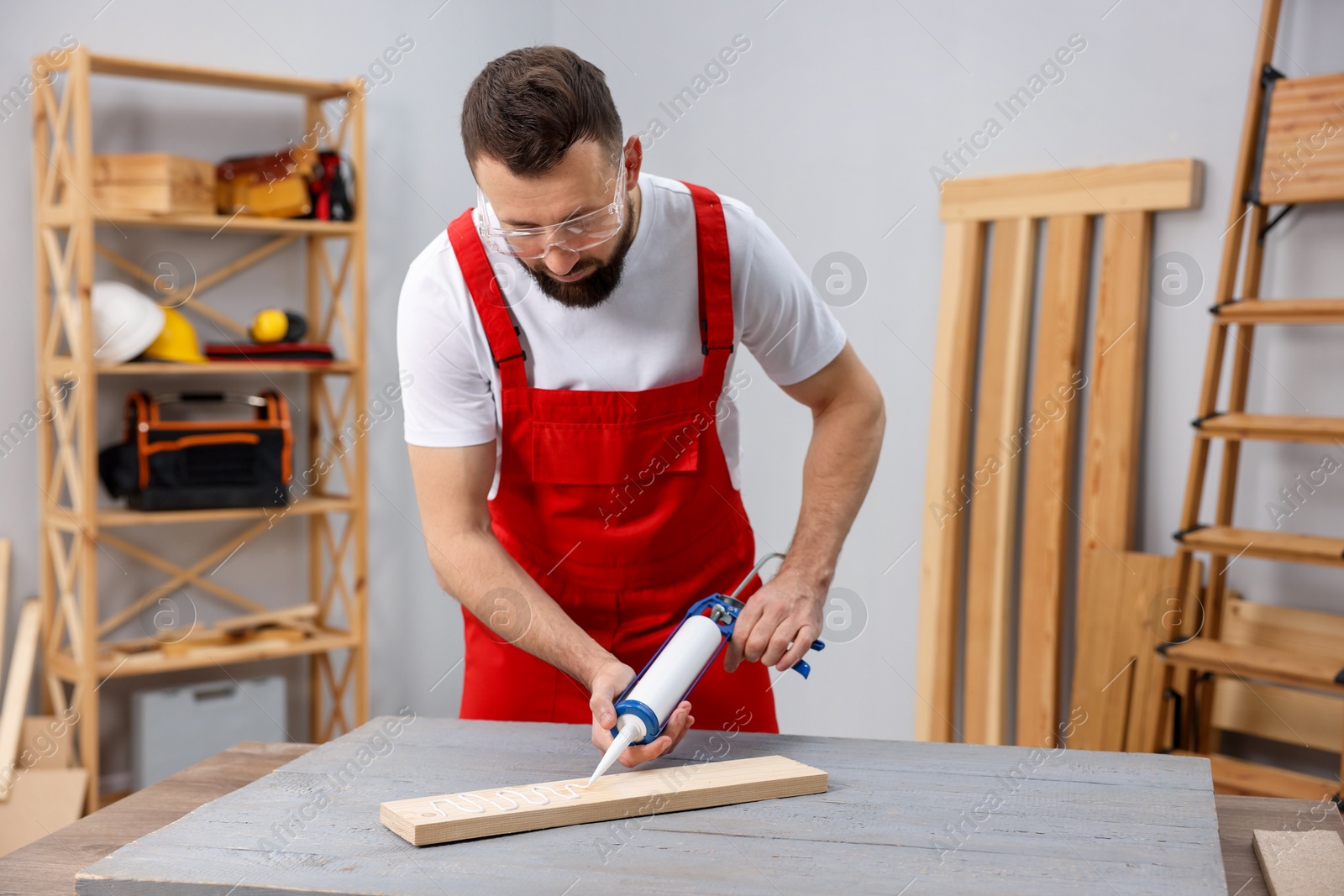 Photo of Worker with caulking gun glueing wooden plank indoors