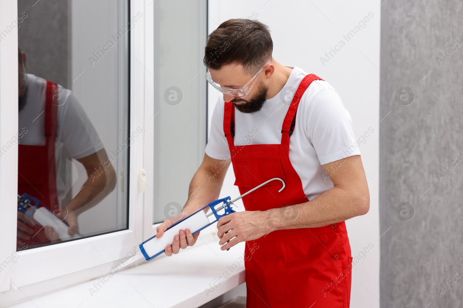 Photo of Worker with caulking gun sealing window indoors