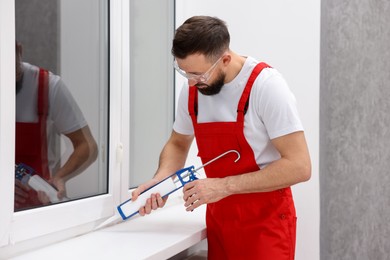 Photo of Worker with caulking gun sealing window indoors