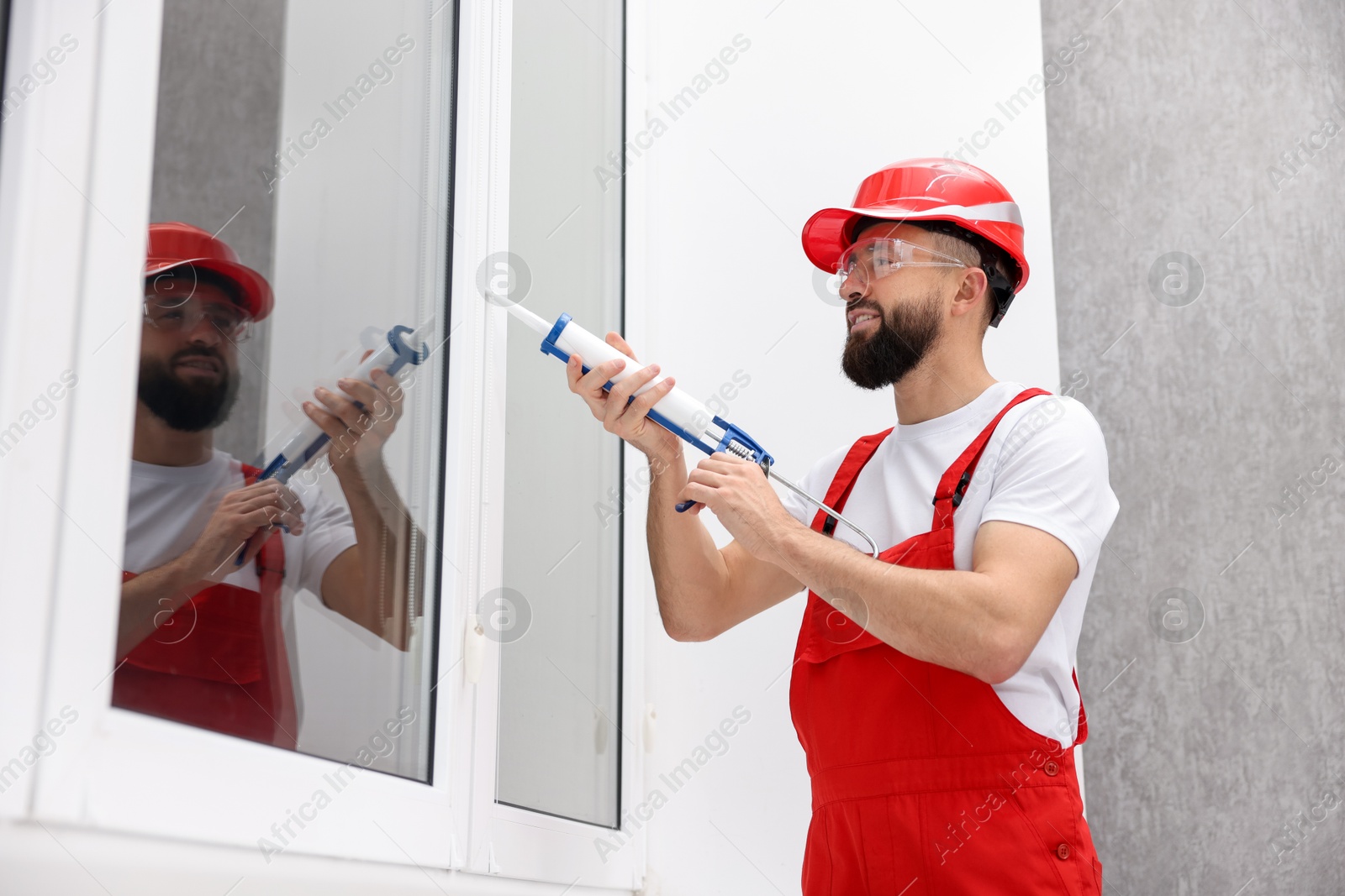 Photo of Worker with caulking gun sealing window indoors, low angle view