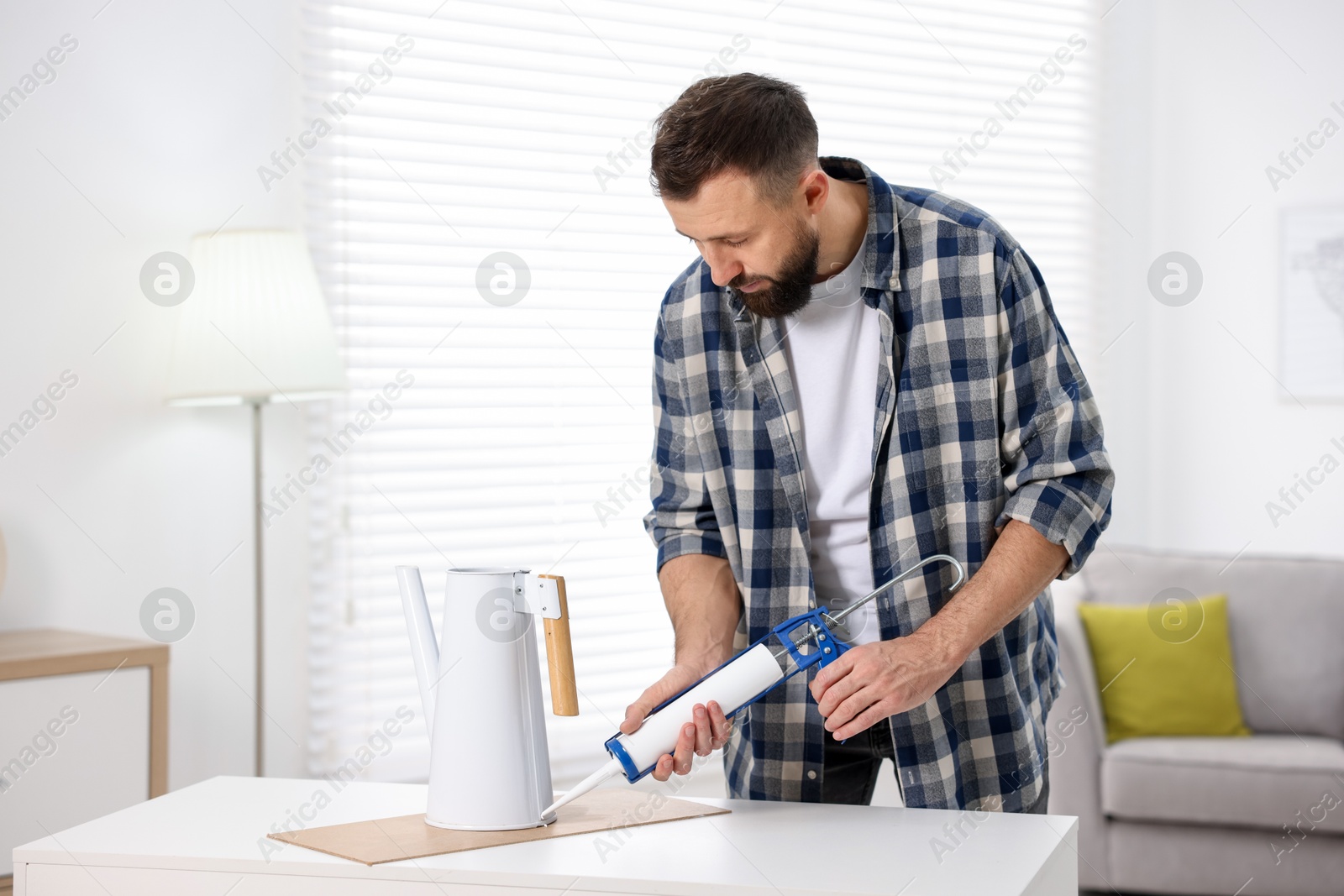 Photo of Man with caulking gun glueing watering can indoors