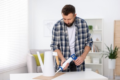 Photo of Man with caulking gun glueing watering can indoors