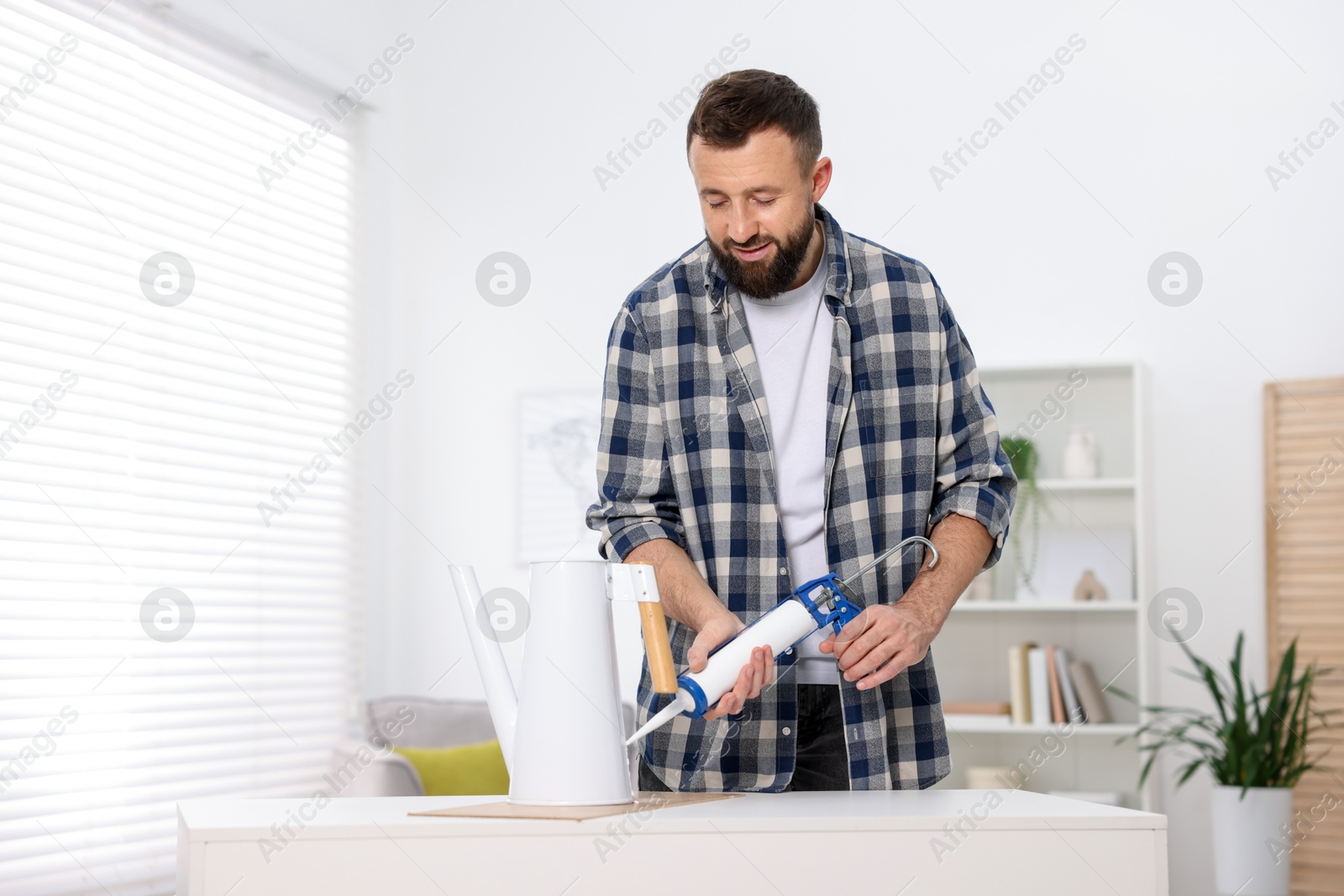 Photo of Man with caulking gun glueing watering can indoors