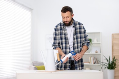 Photo of Man with caulking gun glueing watering can indoors