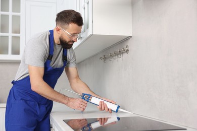 Photo of Worker with caulking gun sealing countertop indoors