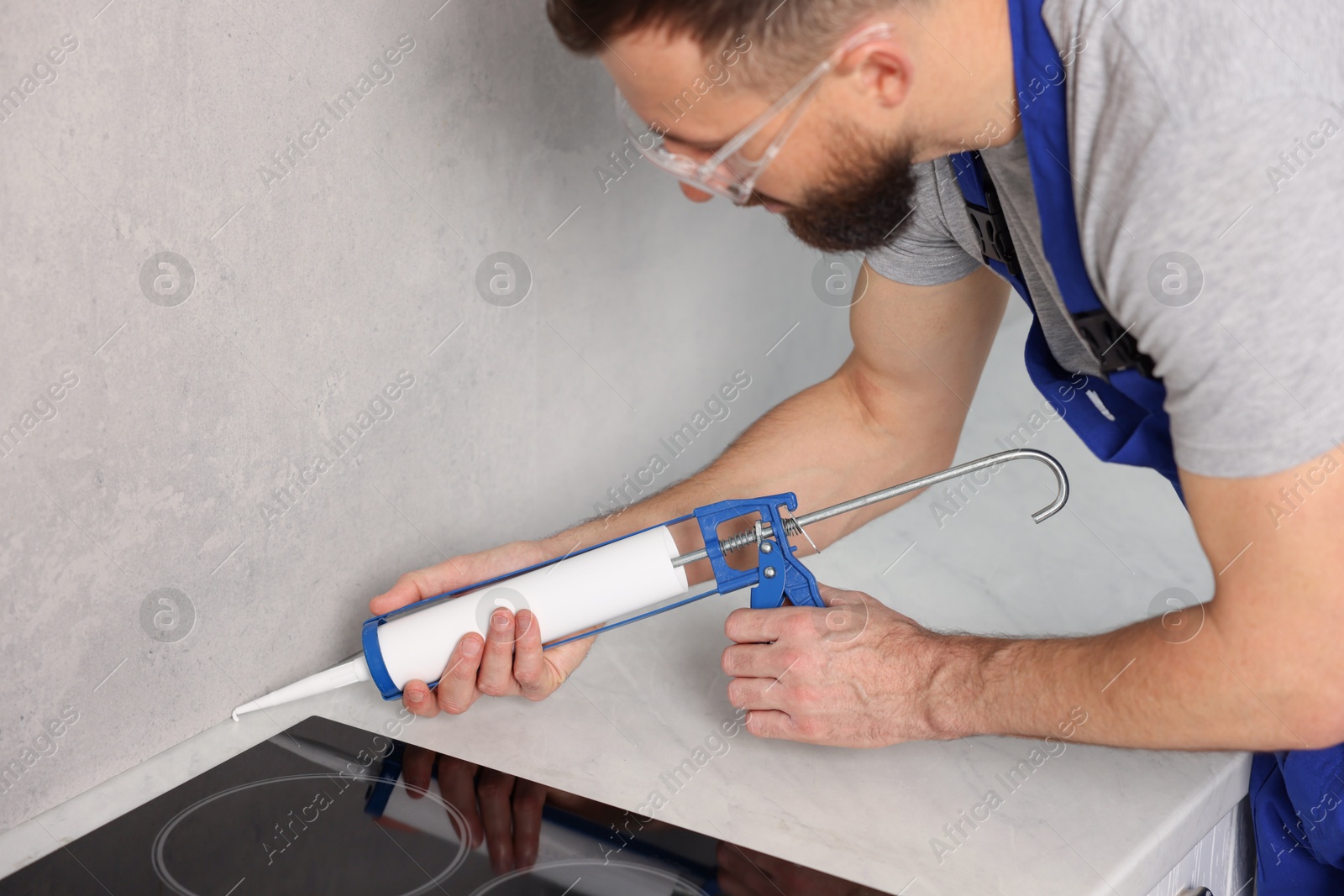 Photo of Worker with caulking gun sealing countertop indoors