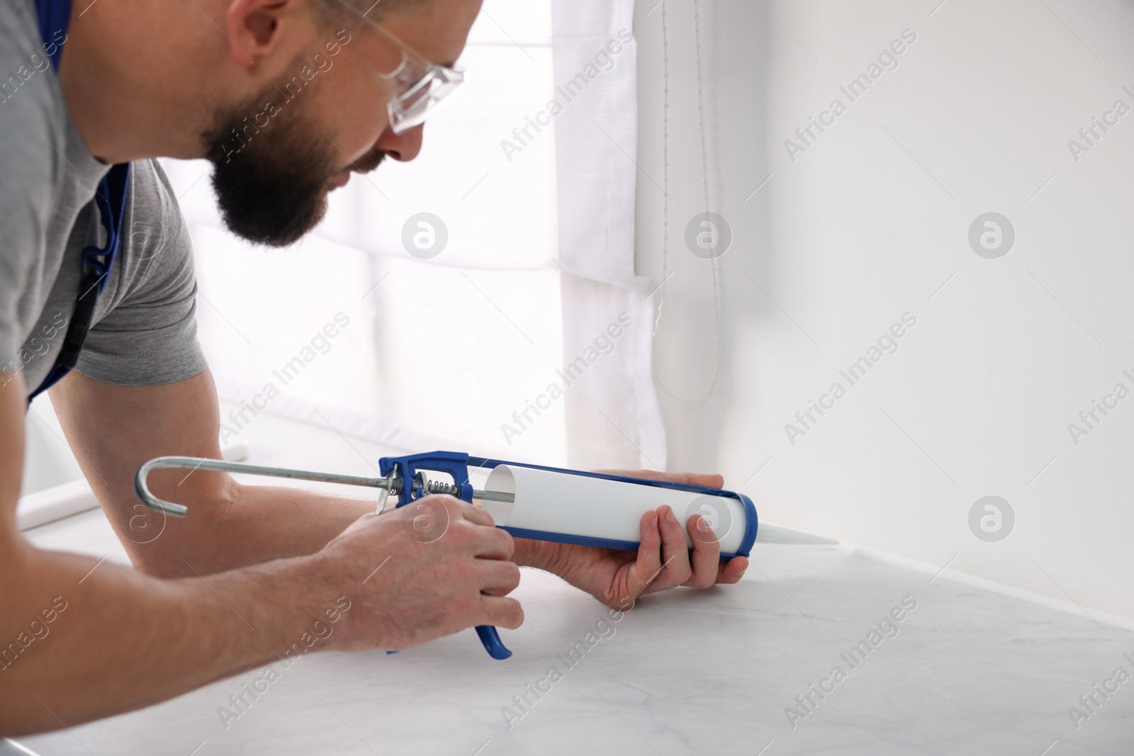 Photo of Man with caulking gun sealing countertop indoors