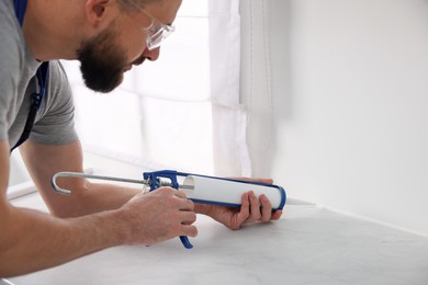 Photo of Man with caulking gun sealing countertop indoors