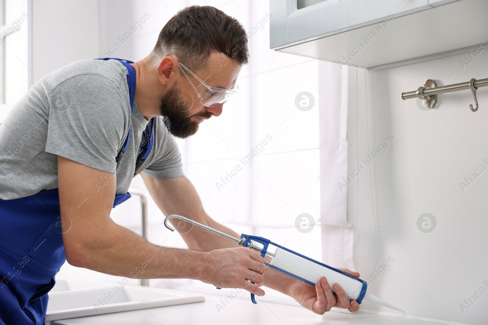 Photo of Worker with caulking gun sealing countertop indoors