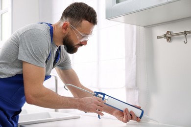 Photo of Worker with caulking gun sealing countertop indoors