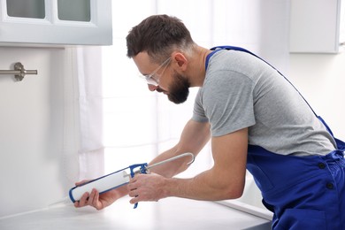 Photo of Worker with caulking gun sealing countertop indoors