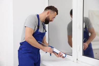 Photo of Worker with caulking gun sealing window indoors