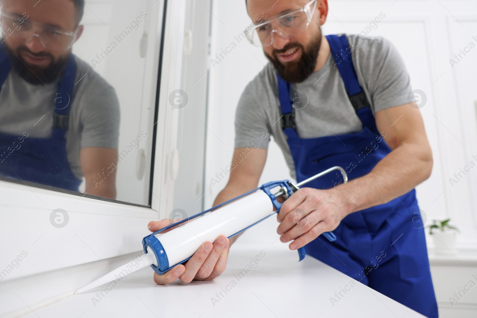 Photo of Worker with caulking gun sealing window indoors, selective focus