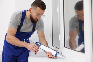 Photo of Worker with caulking gun sealing window indoors