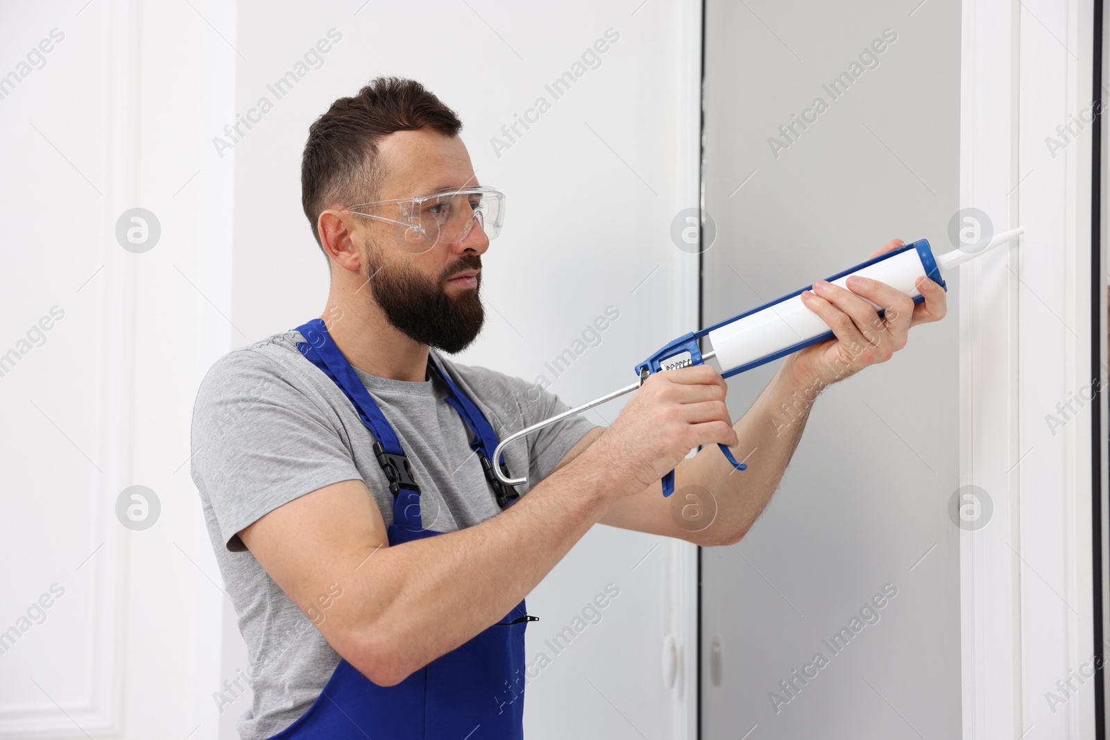 Photo of Worker with caulking gun sealing window indoors