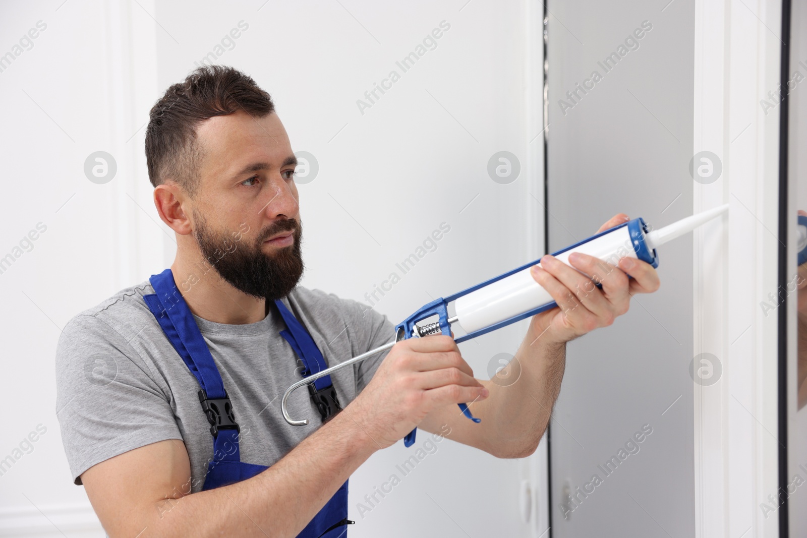 Photo of Worker with caulking gun sealing window indoors