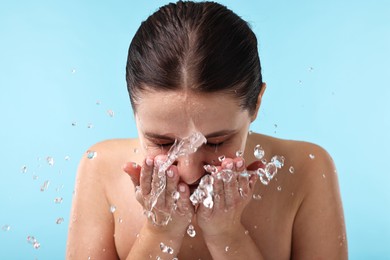 Photo of Woman washing her face on light blue background