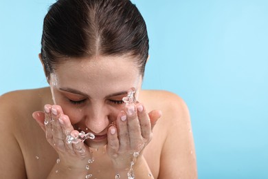 Photo of Woman washing her face on light blue background. Space for text