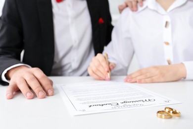 Photo of Newlyweds signing marriage contract and wedding rings on desk, selective focus