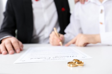 Photo of Newlyweds signing marriage contract and wedding rings on desk, selective focus