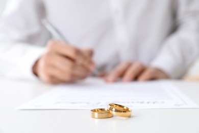 Photo of Man signing marriage contract and wedding rings on desk, selective focus