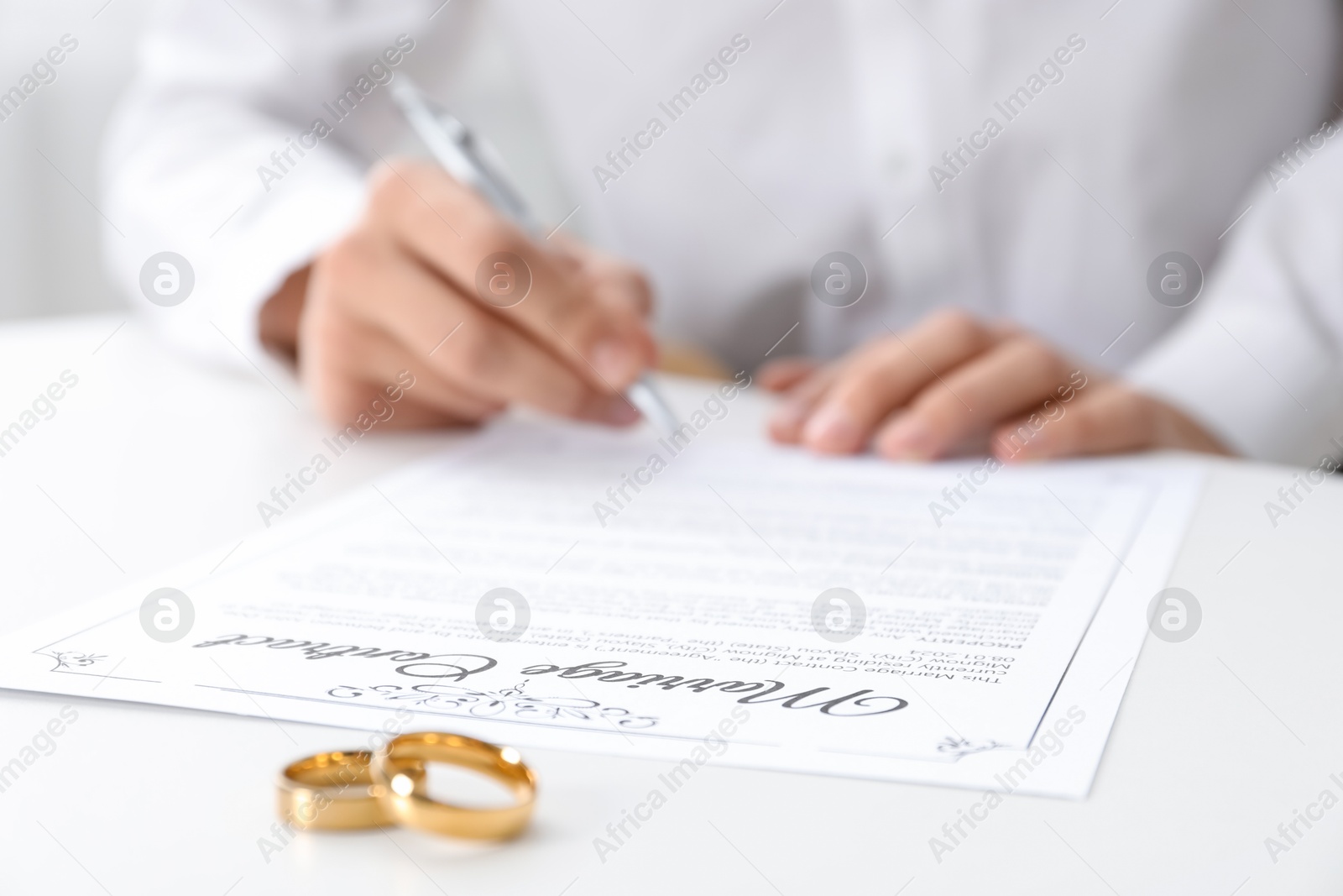 Photo of Man signing marriage contract and wedding rings on desk, selective focus