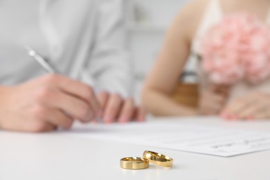 Photo of Newlyweds signing marriage contract and wedding rings on desk, selective focus