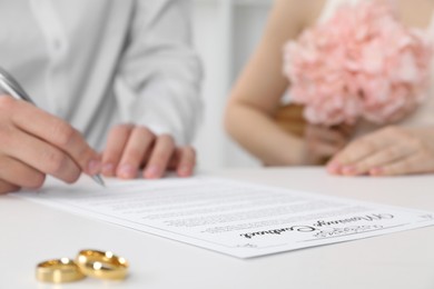 Photo of Newlyweds signing marriage contract and wedding rings on desk, selective focus