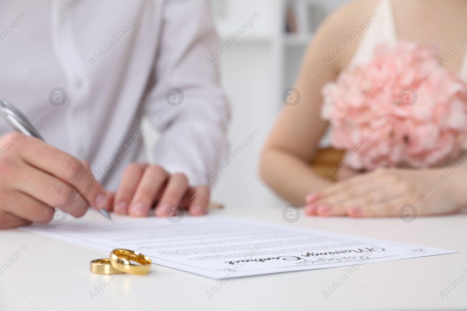 Photo of Newlyweds signing marriage contract and wedding rings on desk, selective focus