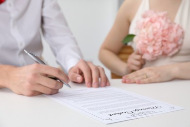 Photo of Newlyweds signing marriage contract at desk, closeup