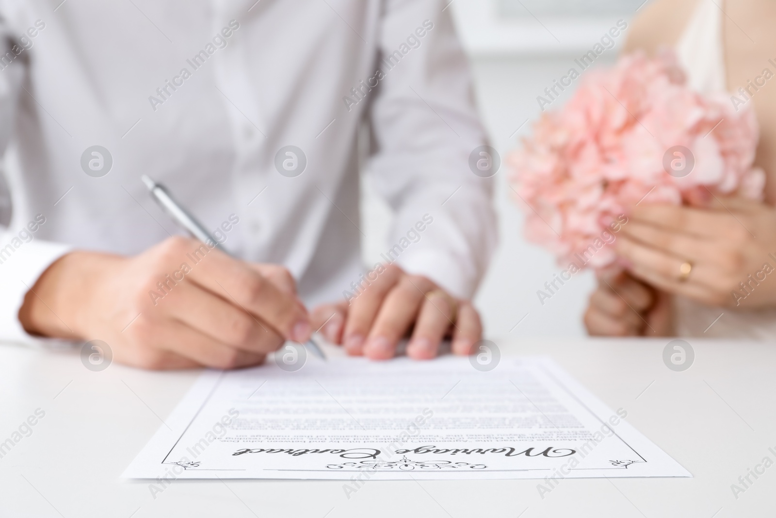 Photo of Newlyweds signing marriage contract at desk, closeup