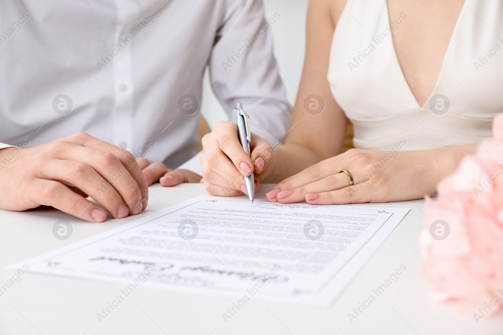 Photo of Newlyweds signing marriage contract at desk, closeup